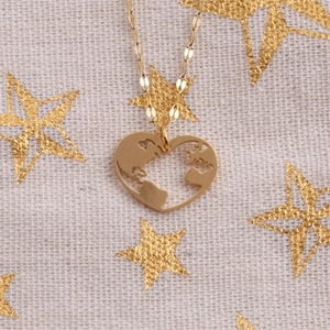 Macro shot of gold heart pendant with hollow world map design on white starry fabric