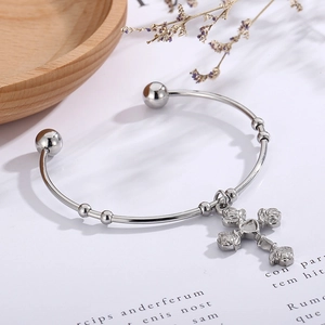 Detail of silver rose-engraved cross pendant on a vintage style open cuff bracelet