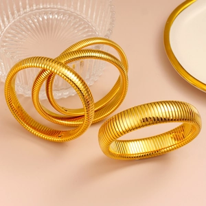 Vista macro de cuatro brazaletes estriados bañados en oro de 18K en una bandeja
