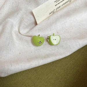 Macro shot of green enamel apple stud earrings on a textured fabric backdrop