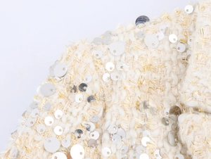 Gros plan sur le tissu en tweed crème avec paillettes argentées et fils dorés