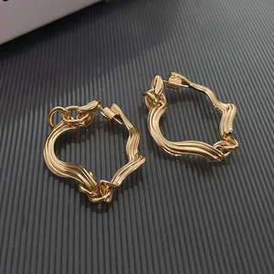 Macro detail of golden geometric twisted earrings on a textured striped background