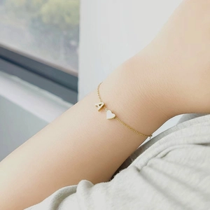 Close-up of a gold chain bracelet with letter A pendant and shell heart charm on wrist