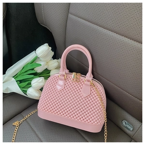 Pink pearl-textured jelly handbag with gold chain strap placed on a luxury car seat