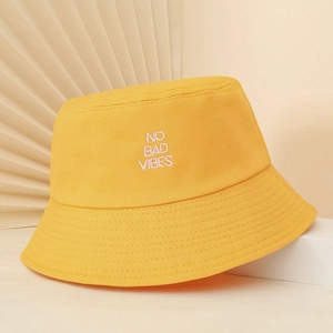 Detail of yellow canvas bucket hat with NO BAD VIBES white letter embroidery on a white stand