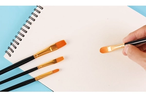 Action shot of blue nylon paintbrushes with gold ferrules used on a white sketchbook