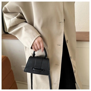 Detail of black mini handbag with lychee leather texture and curved bottom design
