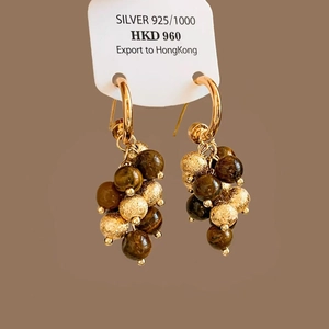 Detail of 925 silver tiger eye drop earrings with geometric gold and brown beads