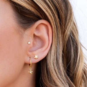 Detail of gold star earring set with zircon pendants worn on model's ear