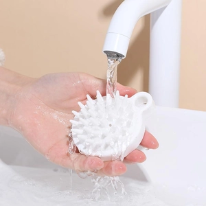 White silicone scalp massager hair brush being rinsed under running water for easy cleaning