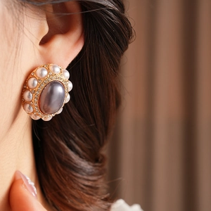 Close-up of vintage oval earring with grey stone, pearls and crystals on a model