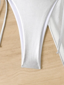 Detail of silver metallic bikini fabric with fine stitching and side tie on wood surface