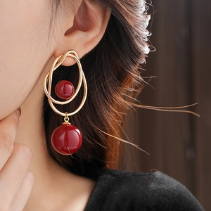 Close-up of geometric gold wire earrings featuring two vibrant red spherical charms