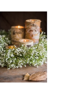 Macro detail of birch bark candles and white floral wreath on rustic wooden table