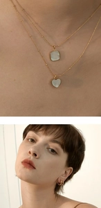 Detail of double-layer gold necklace with square and heart mother of pearl pendants