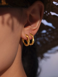 Gros plan sur les créoles géométriques torsadées dorées portées sur une oreille