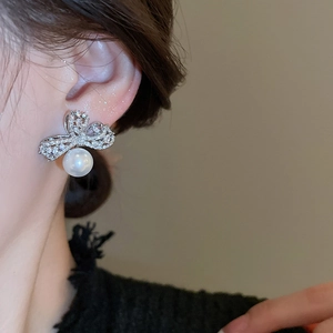 Close-up of bow knot stud earring with pavé diamonds and a white pearl drop