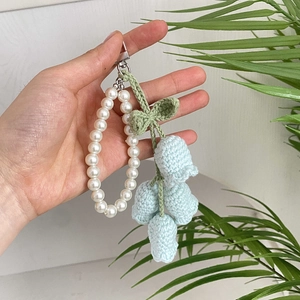 Macro shot of hand-crocheted light blue lily of the valley charm with pearl wrist strap