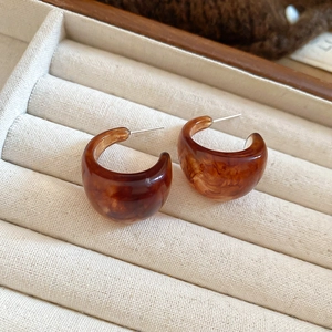 Macro view of C-shaped resin amber earrings with vintage tortoise shell texture on beige velvet