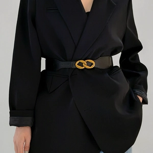 Detail view of a black leather elastic waist belt with a golden interlocking buckle on a blazer