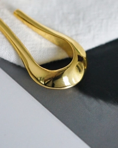 Detailed close-up of a minimalist U-shaped gold-plated hair pin with a polished mirror finish