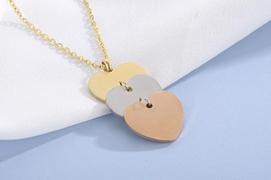 Détail des pendentifs en forme de cœur superposés en or, argent et or rose sur une chaîne