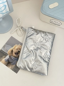 Detail of silver metallic bow-embossed pouch with a white zipper and pearl bow charm