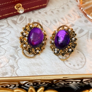 Detail of vintage gold-tone clip-on earrings with oval purple gems and white seed pearls