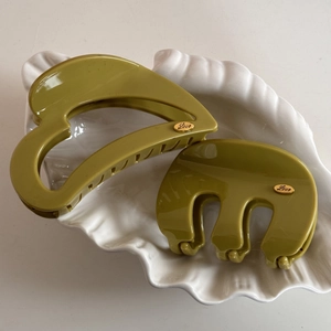 Detail of green hair clips in shell tray with gold Love tag on polished surface