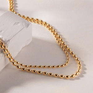 Close-up of golden stainless steel double layer bean necklace on a textured stone
