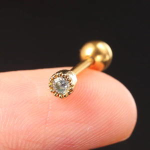 Macro shot of a tiny gold stainless steel screw-back earring with a clear zircon on a fingertip