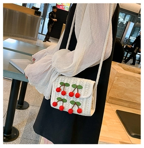 Detail of a white woven straw bag with red cherry accents and a green leaf embroidery