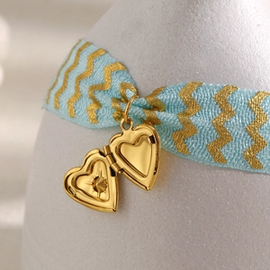 Gold heart locket pendant with blue printed silk ribbon on a white textured vase