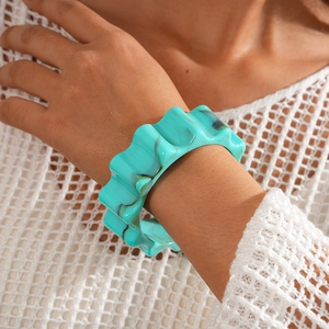 Close-up of blue-green wavy resin bangle on a model wrist with a textured white background