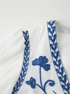 Close-up of blue floral embroidery and ethnic patterns on a white long sleeve cardigan