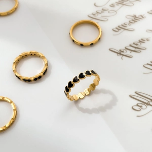 Detailed view of gold rings with black enamel hearts and inlaid square crystals