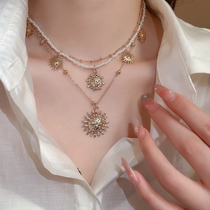 Close-up of layered gold sun pendant necklace with pearls on a white silk shirt