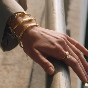 Outdoor view of layered gold-tone chain bracelets and a shimmering dual-stone open ring