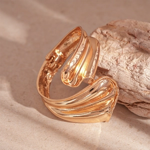 Detail of heavy metal wavy gold cuff bracelet on stone and wood aesthetic background