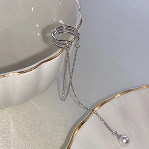 Silver fringe ear cuff with long chain and pearl hanging on a decorative ceramic bowl