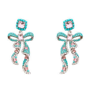 Boucles d'oreilles nœud argenté avec zircons roses et perles turquoise sur fond blanc