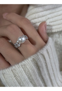 Close-up of white pearl ring with silver lace band on finger with blurred sweater background