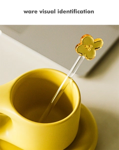 Macro detail of amber flower glass stir stick resting in a yellow ceramic coffee mug