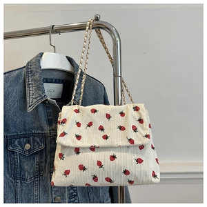 Detail of beige corduroy shoulder bag with strawberry print and gold chain strap