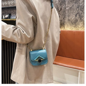 Dettaglio mini borsa a tracolla verde petrolio con catena dorata su blazer grigio