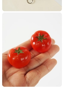 Detailed view of two realistic mini red PVC cherry tomato models held in a hand