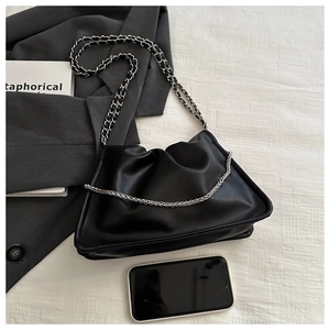 Detail of black pleated cloud bag with silver chain strap on grey blazer fabric