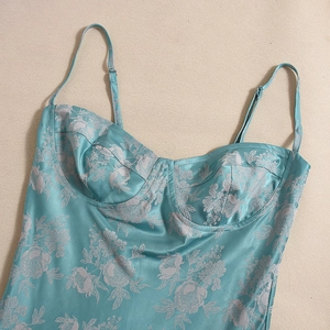 Detail of teal floral satin dress with thin straps and silk texture on beige backdrop