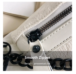 Detail showing the white textured fabric, smooth black metal zipper and chunky chain strap