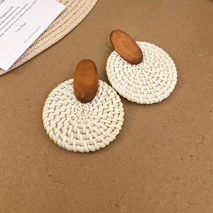 Détail de boucles d'oreilles bohèmes en raphia tressé avec clous en bois sur fond brun